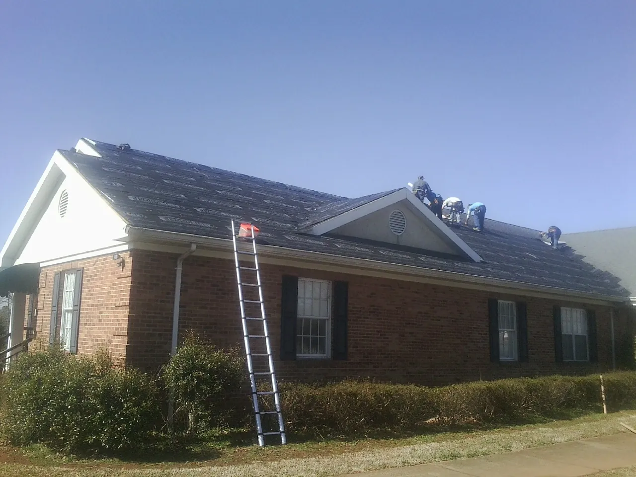 Crew tearing shingles off a brick ranch roof with a ladder set — Metal Roof Repair work by our crew in Calhoun