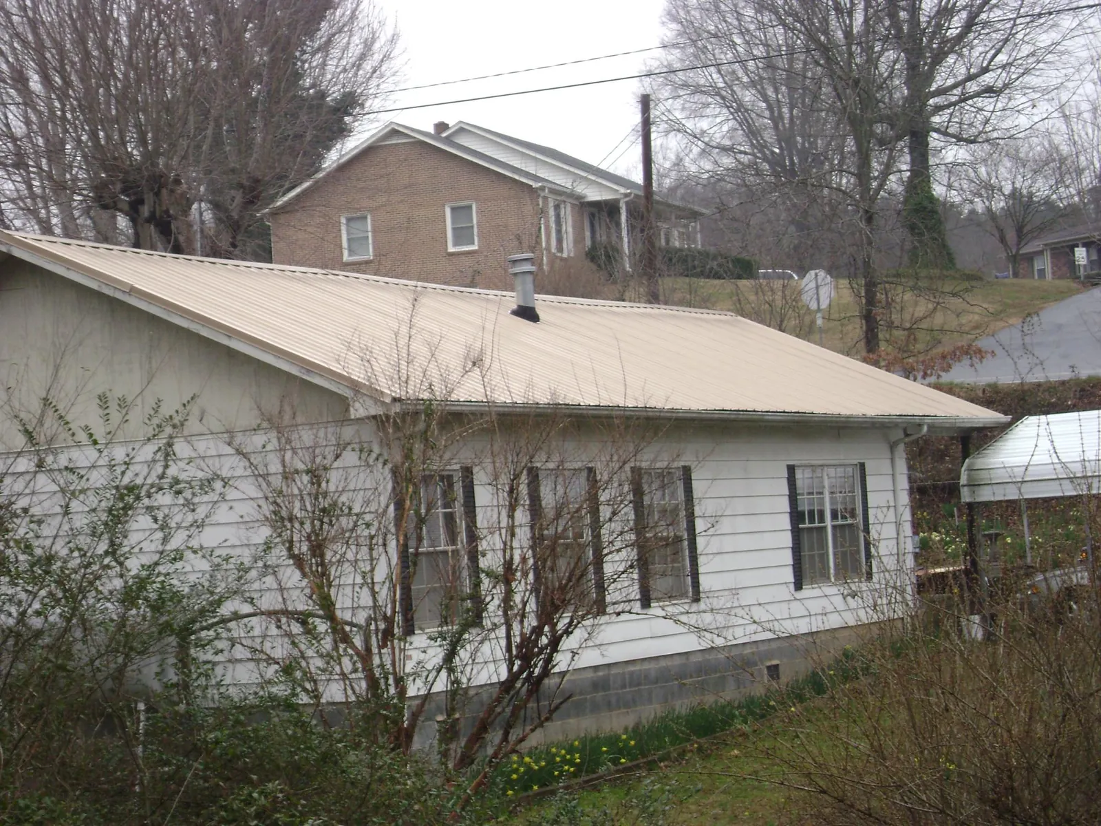 Tan metal roof on a white sided house set into a hillside — Commercial Roofing by Roofing Brothers in Calhoun